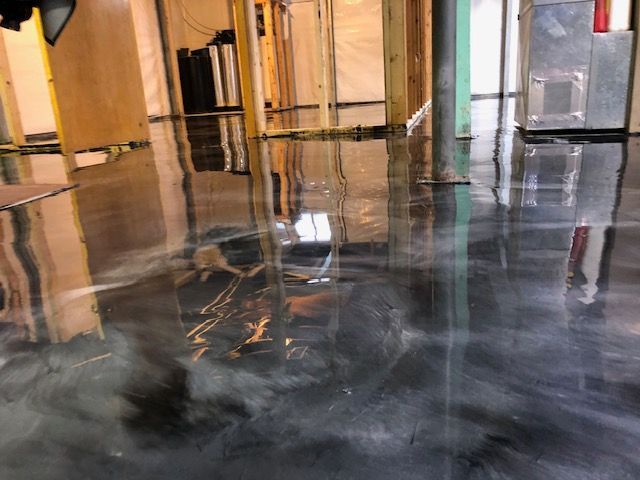 Shiny epoxy floor in a basement, reflecting surrounding construction materials and light. Silver, grey and black colors.