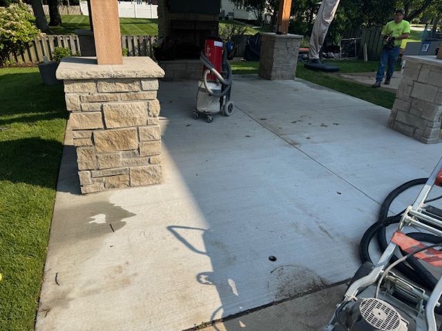 Concrete patio with stone pillars, power tools, and a worker.