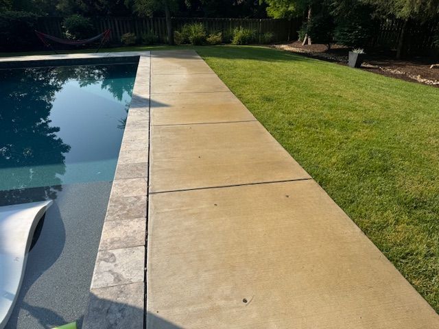 Concrete walkway next to a swimming pool and green lawn.