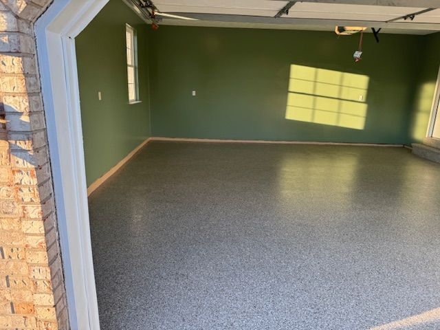 Empty garage with epoxy floor, olive green walls, and sunlight streaming through windows.