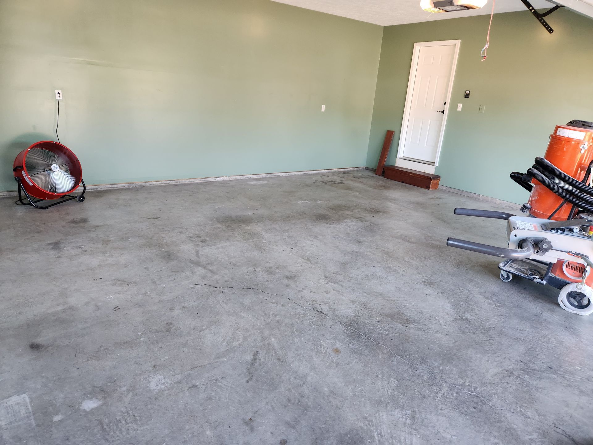 Empty garage with light green walls and a concrete floor. A fan and a machine are visible.