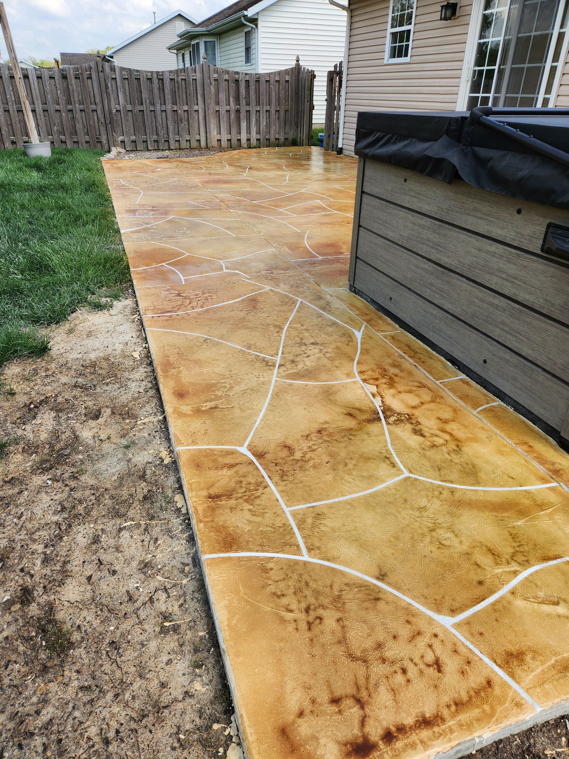Decorative concrete walkway in a backyard, featuring stone pattern with brown and tan colors.