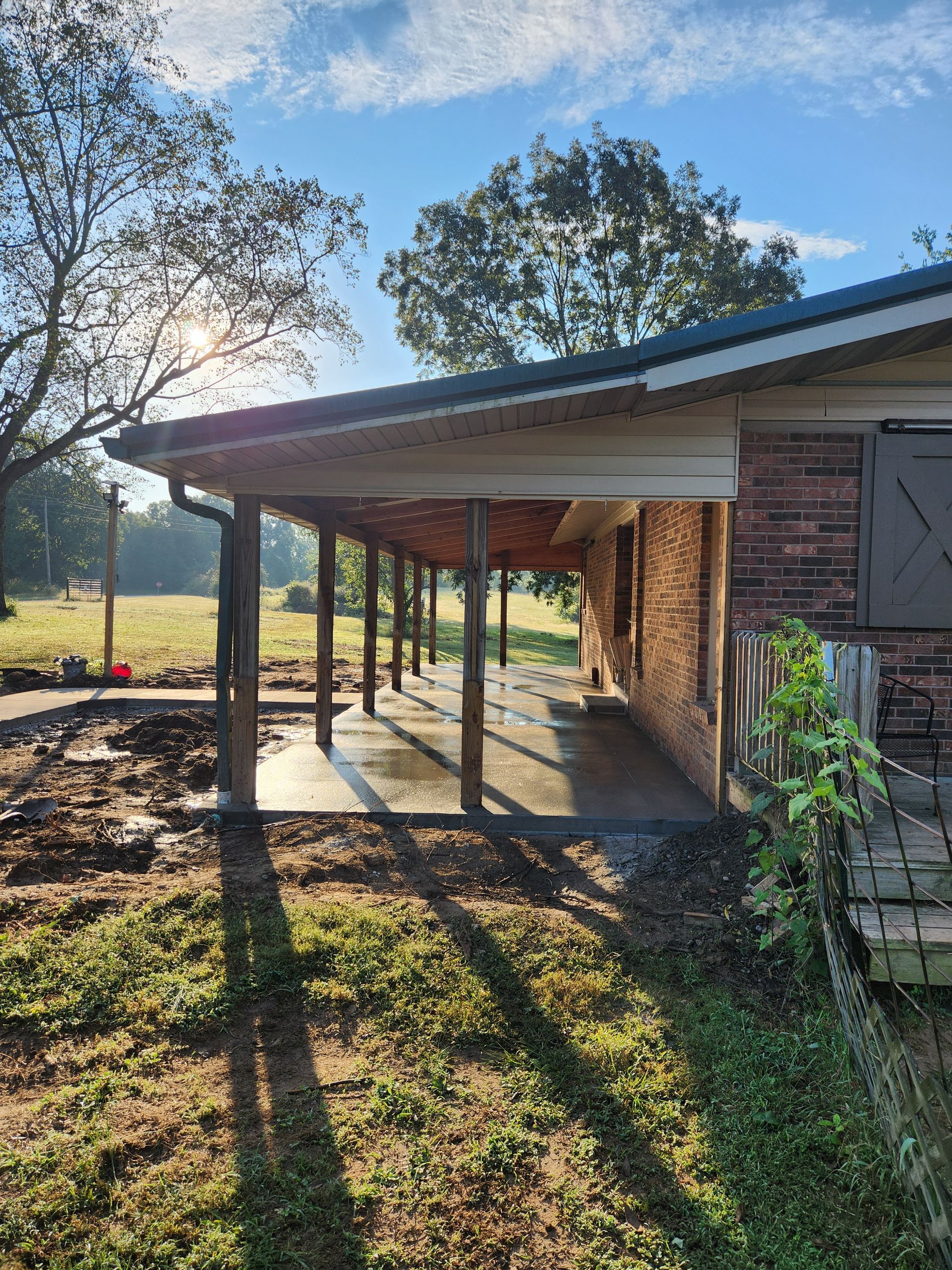 A low-slung brick building with a covered porch casting shadows on a grassy yard.