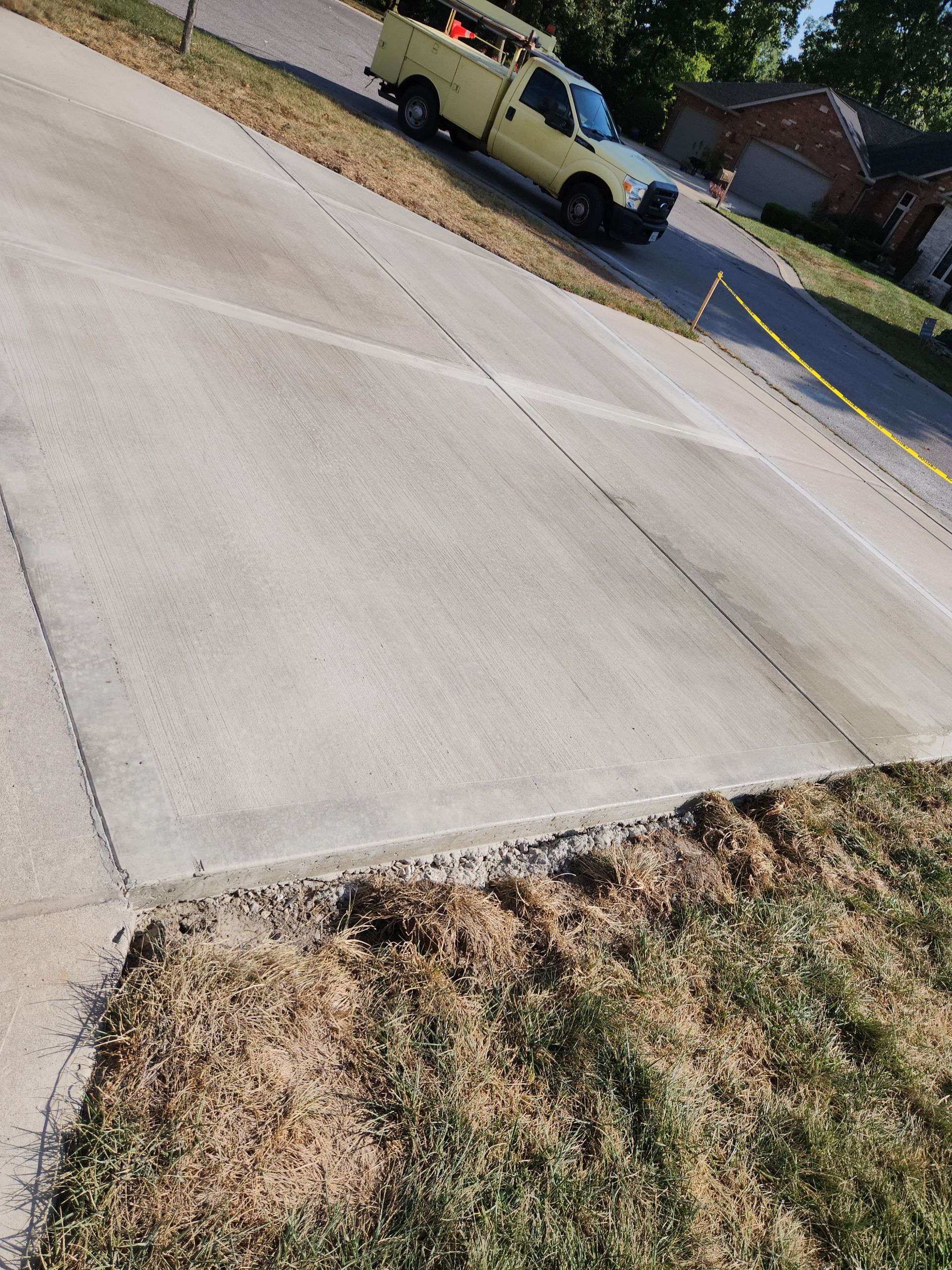 Concrete driveway with work truck parked on it, yellow caution tape to the side.