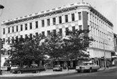 A black and white photo of a large building with cars parked in front of it.