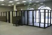 A large room with a lot of glass doors and cubicles.
