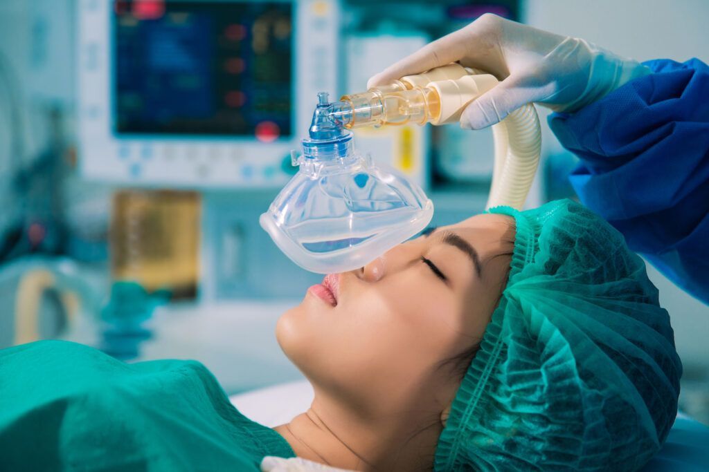 Patient in surgical cap receiving anesthesia through a mask in a medical setting
