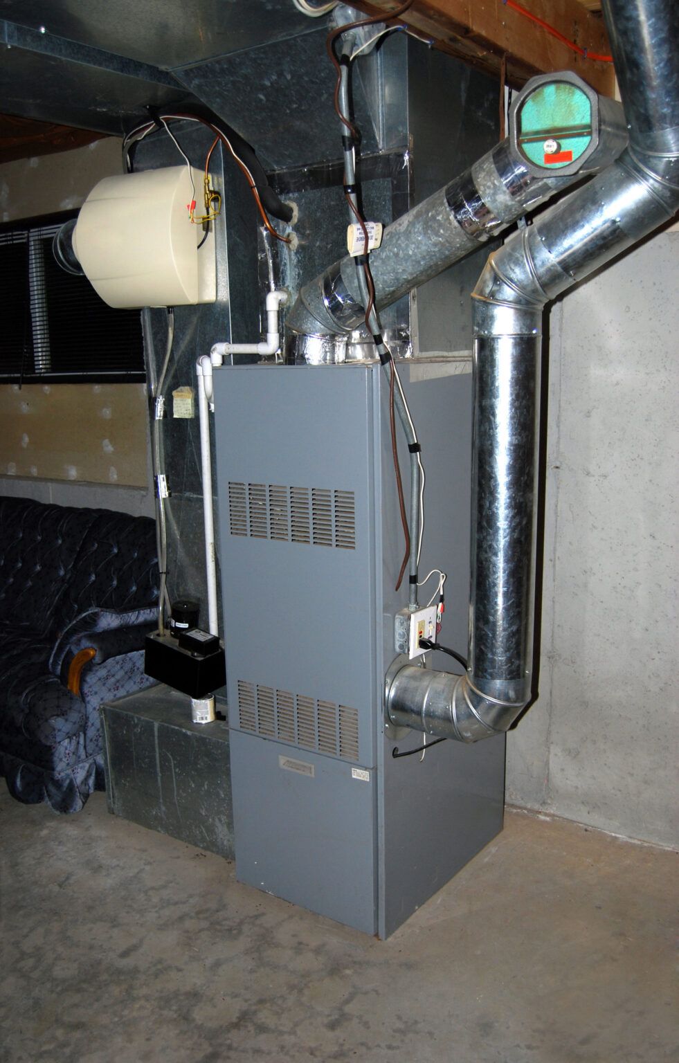 Basement furnace with metal ducts and pipes beside a concrete wall