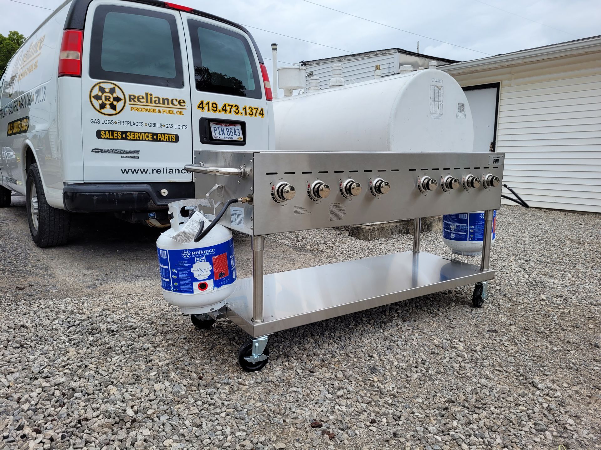 Stainless steel outdoor grill on gravel beside a white van and building, with paint cans on each end.