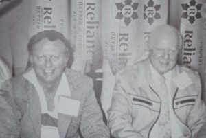 Two smiling people seated in front of branded event banners, black-and-white photo