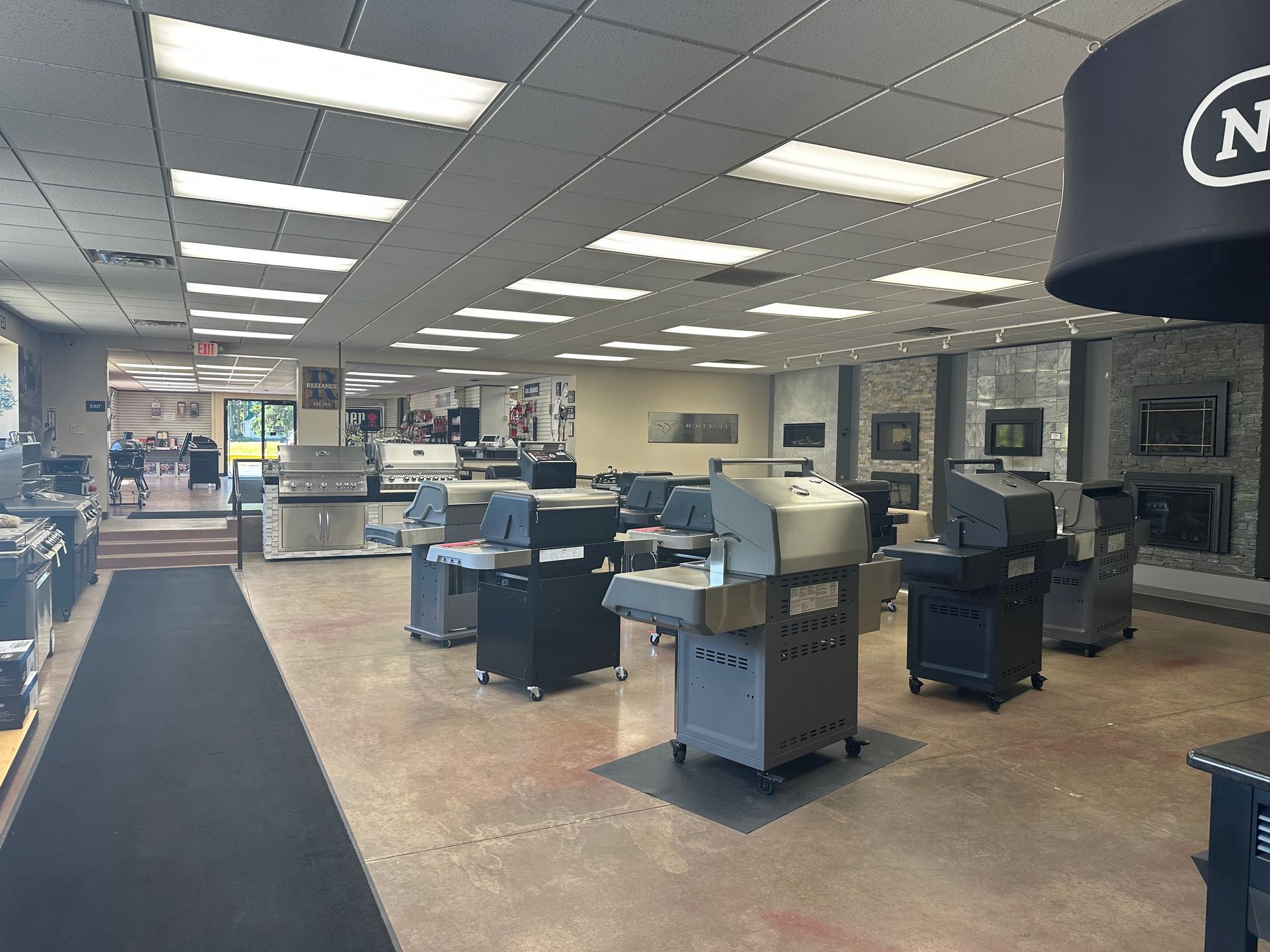 Retail store interior with display counters, appliances, and a dark carpeted aisle under bright ceiling lights.