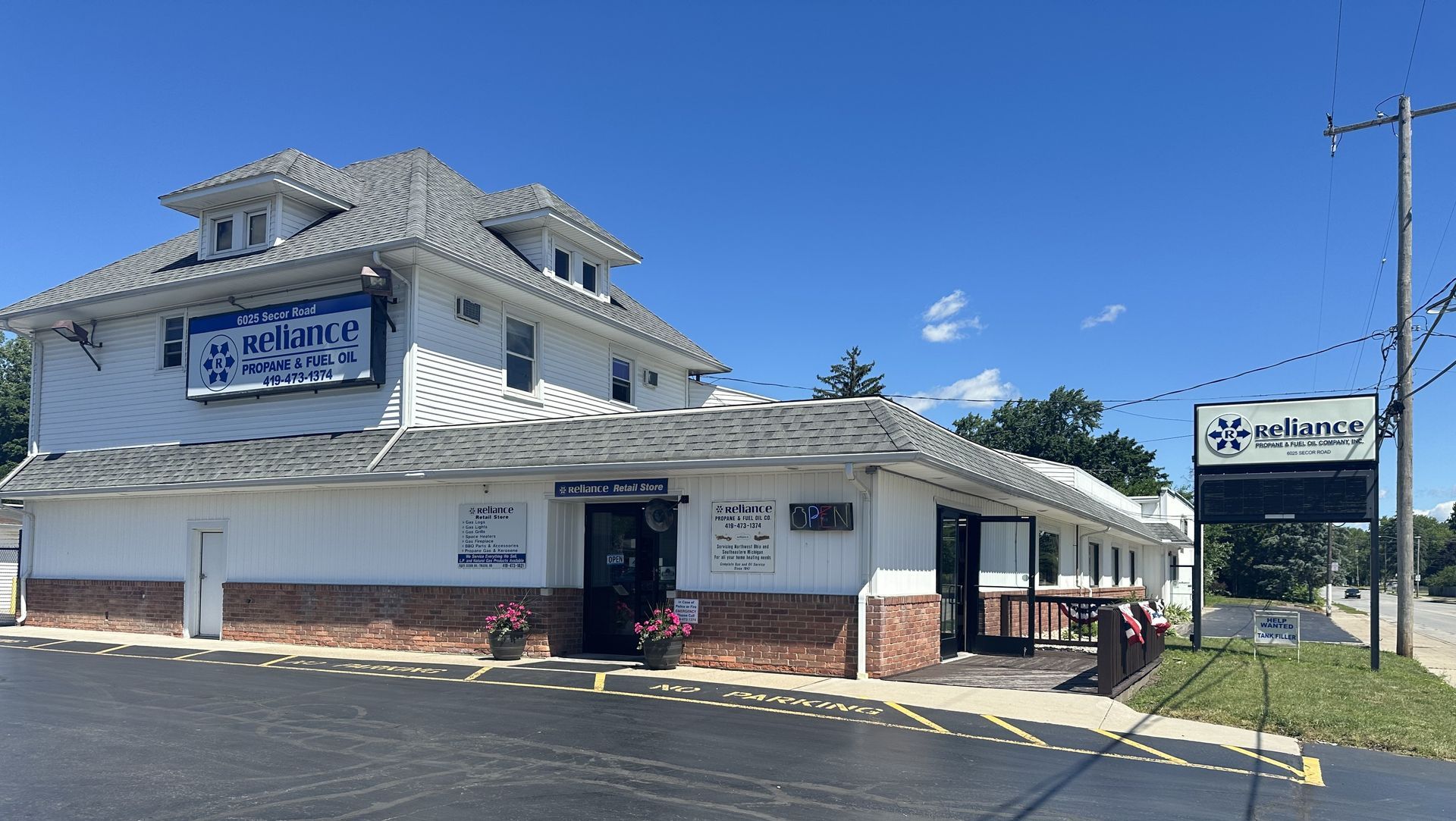Exterior of a white two-story building with a sign, dark roof, and clear blue sky on a sunny day