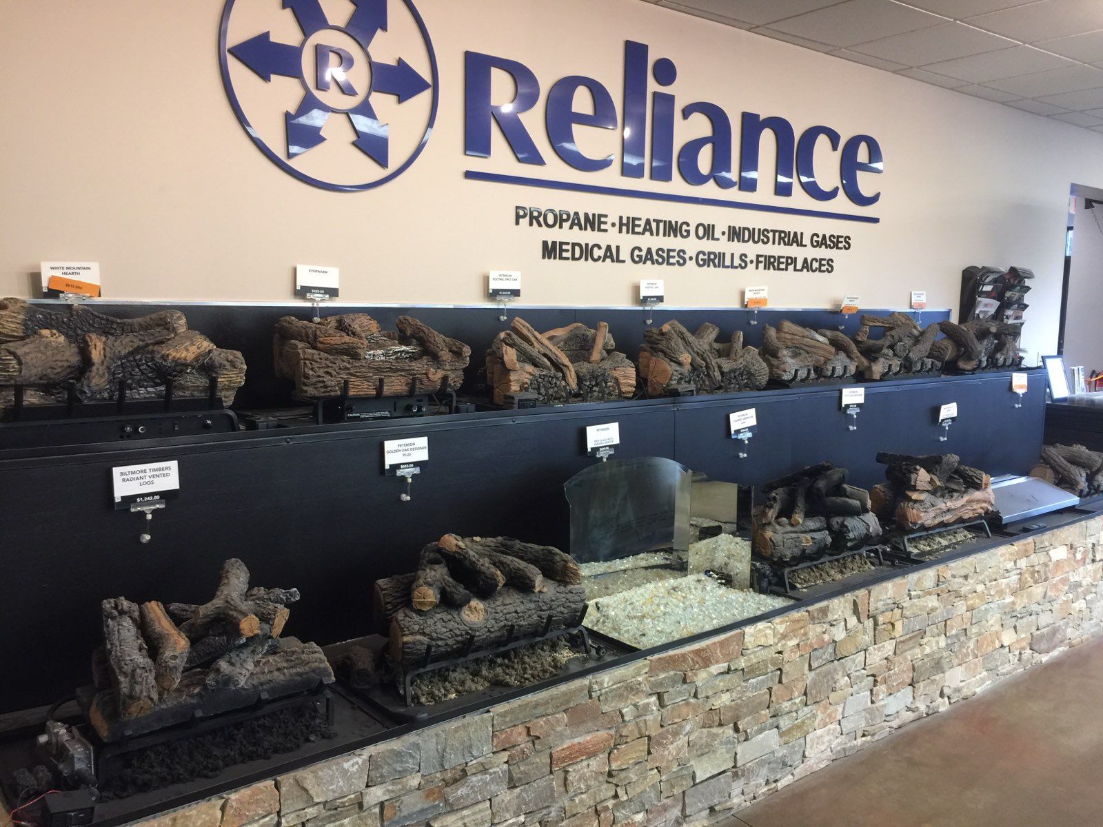Stone fireplace display in Reliance Propane and Medical Gas showroom with black panels and stacked logs