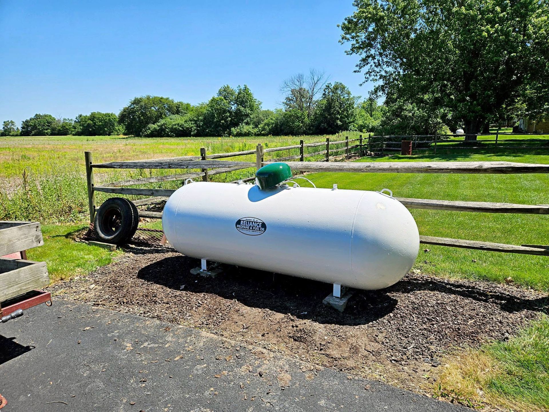 White propane tank on a trailer in a grassy field under a clear blue sky.