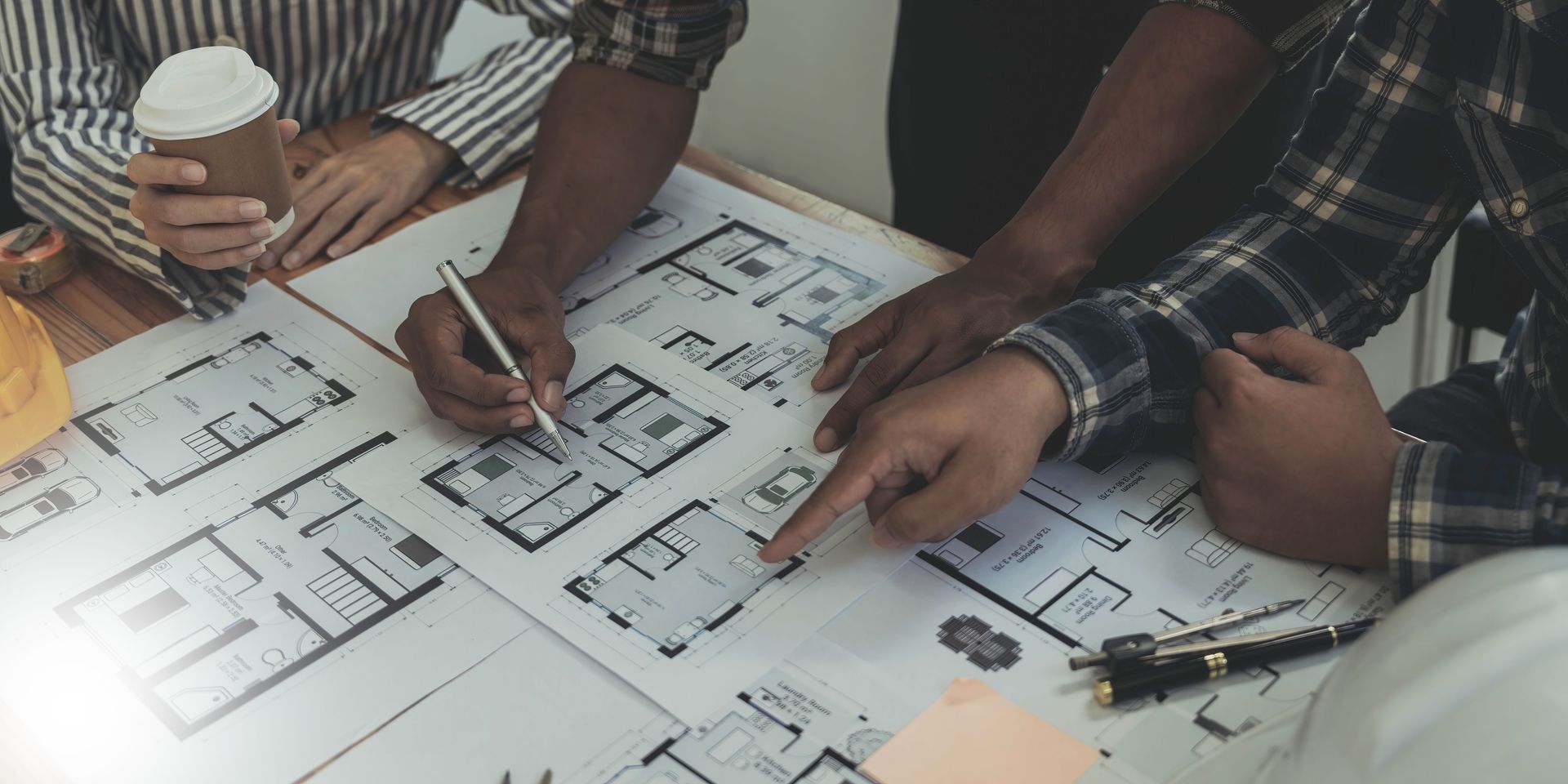 Architects reviewing building plans at a desk, with coffee and tools.