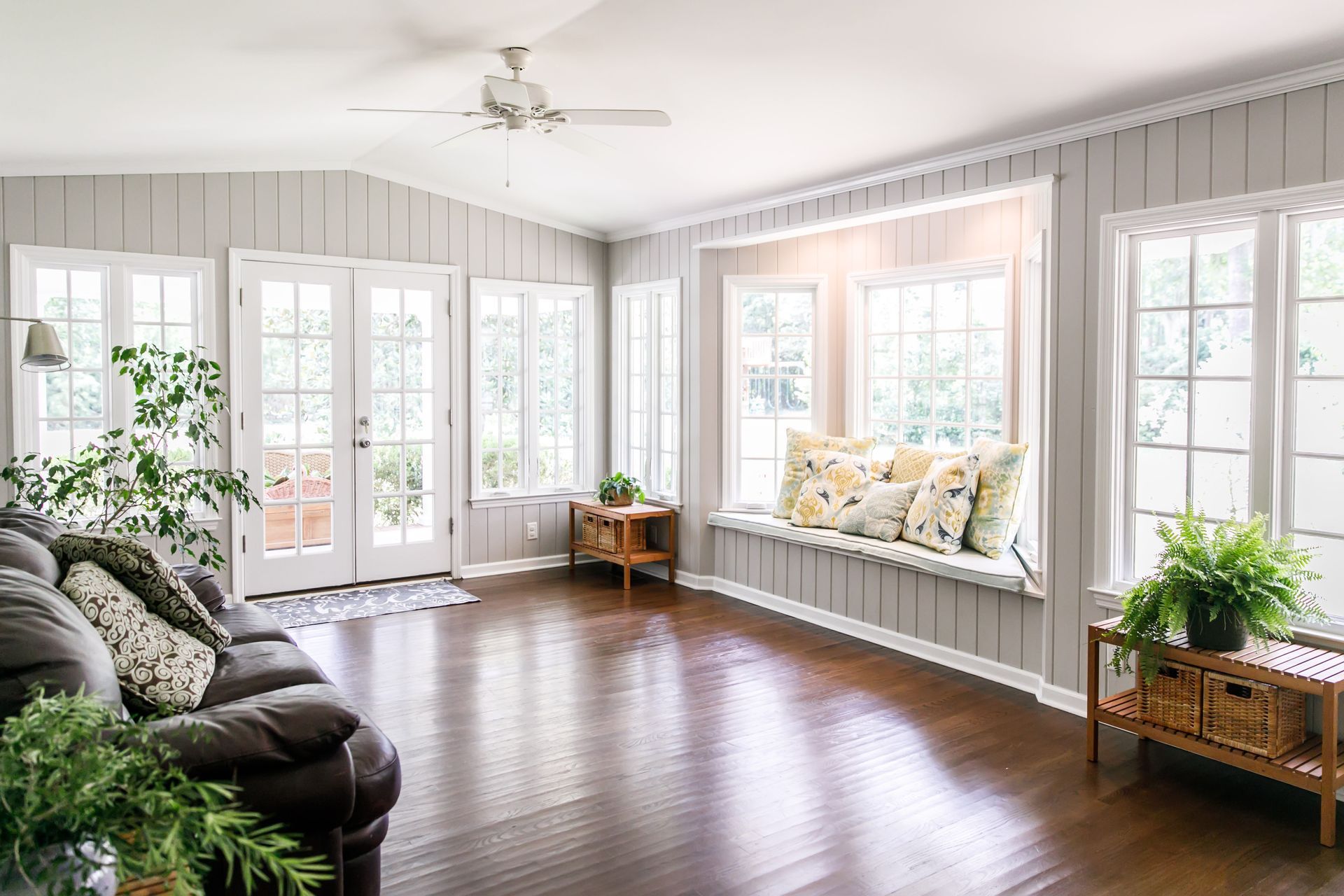 Living room with a dark wooden floor, gray walls, large windows, and a built-in window seat.