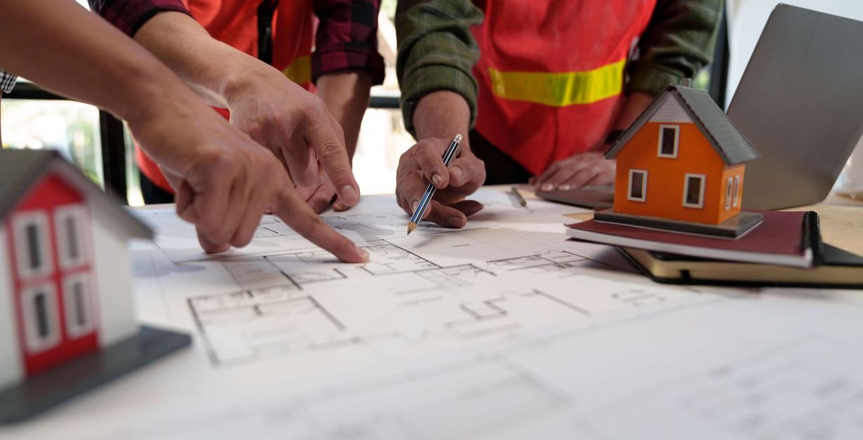 Construction workers examining blueprints with house models and a laptop.