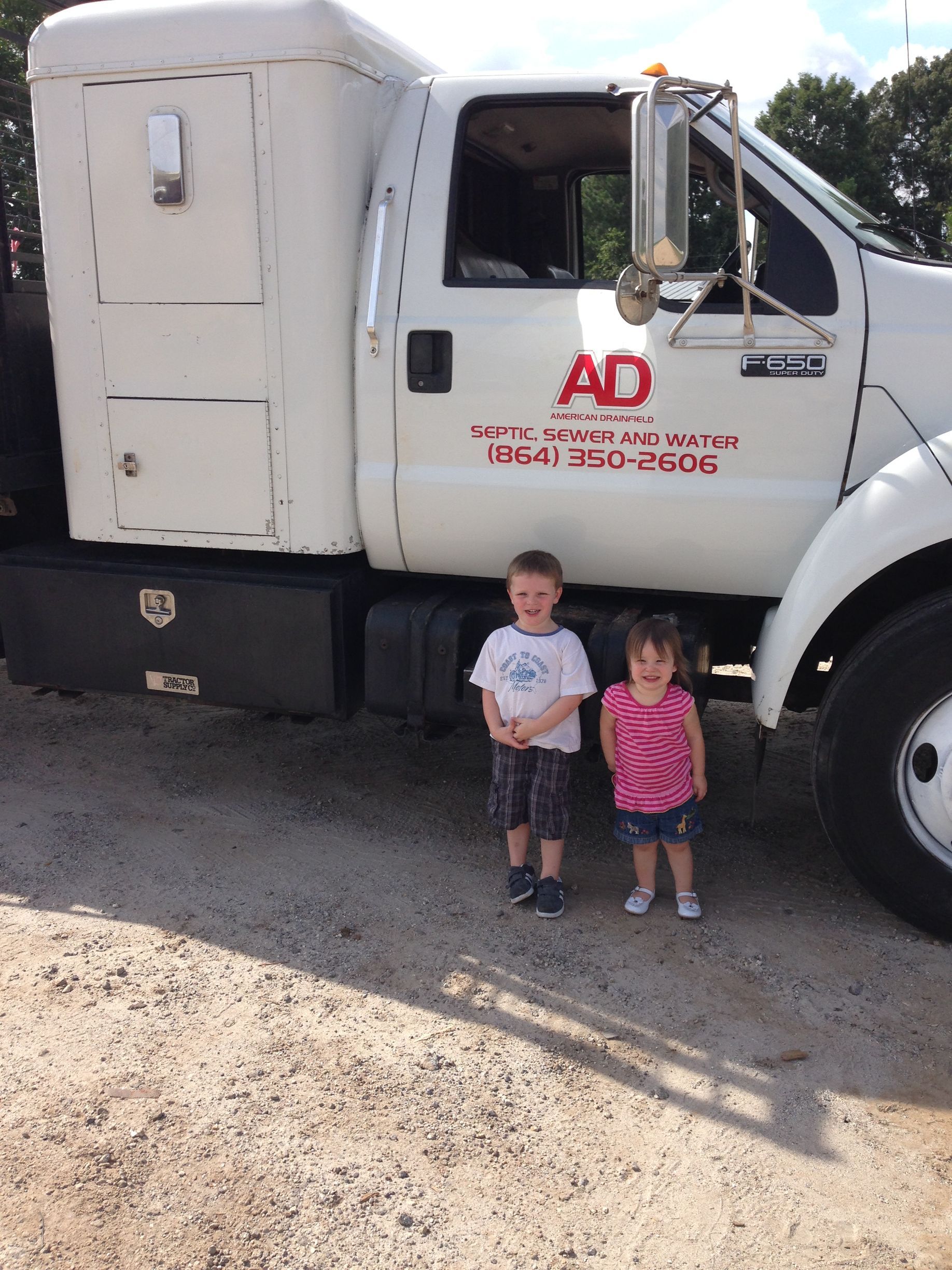 Two children standing beside a white AD truck in a gravel lot.