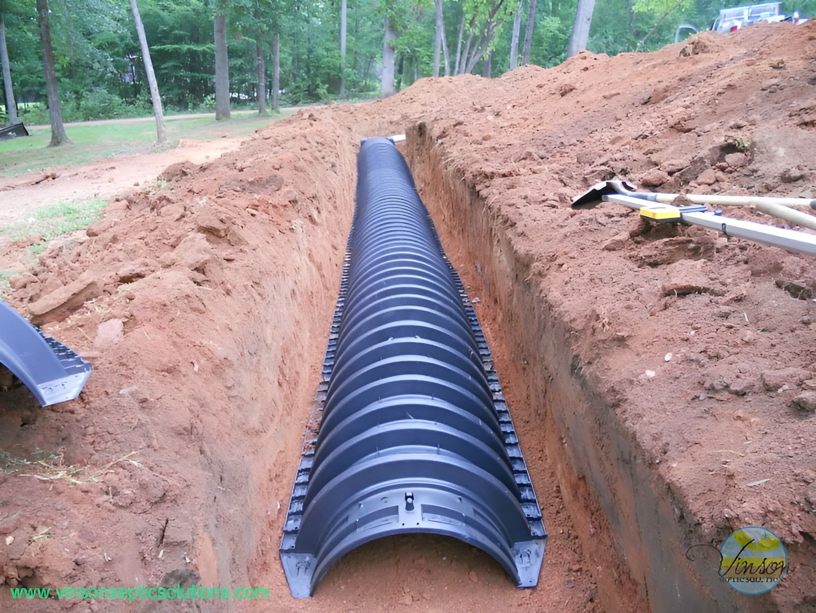 Black plastic drainage pipe installed in a long dirt trench at a construction site.