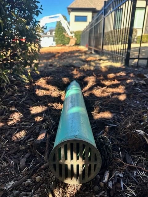 Green drainage pipe lying on mulch beside a building fence in a landscaped yard
