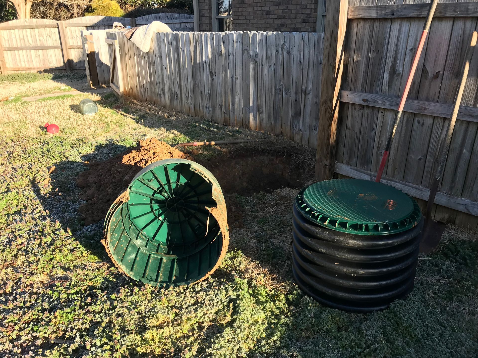 Green underground plastic chamber components in a backyard beside a wooden fence.