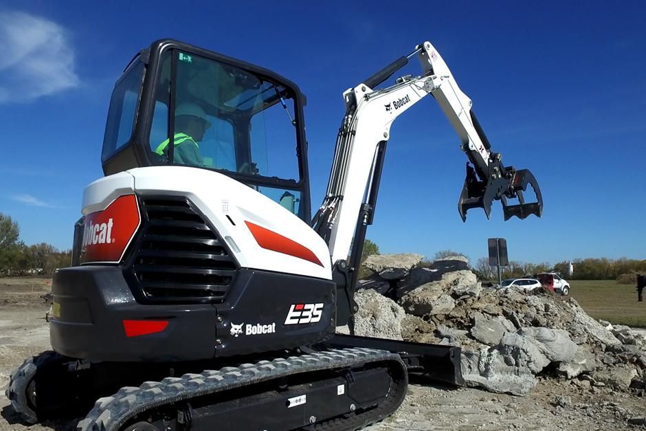 A bobcat excavator is sitting on top of a pile of rocks.