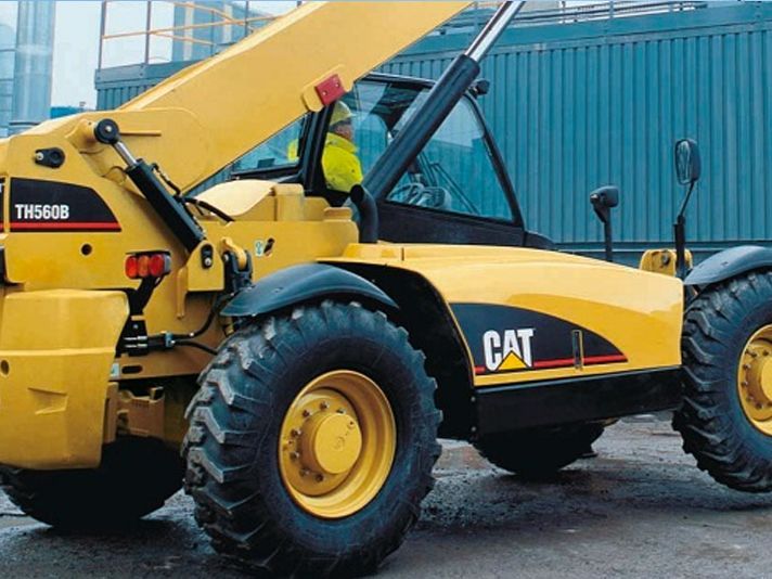 A yellow cat tractor is parked in front of a blue building