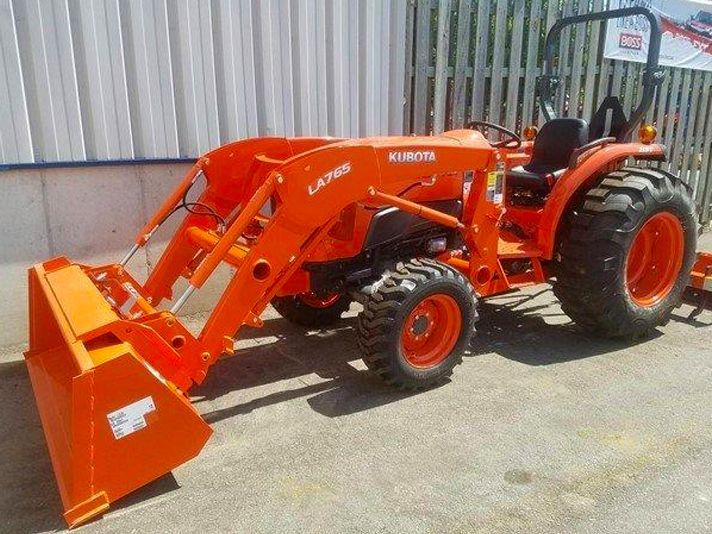 An orange tractor with a bucket attached to it is parked in front of a building.