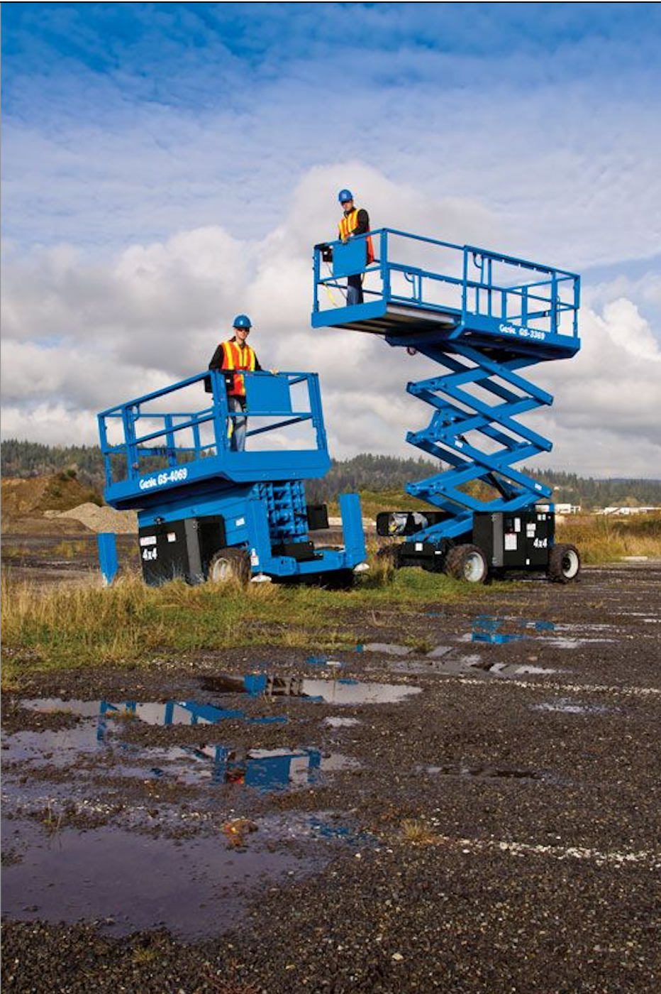 Two men are standing on scissor lifts in a muddy field