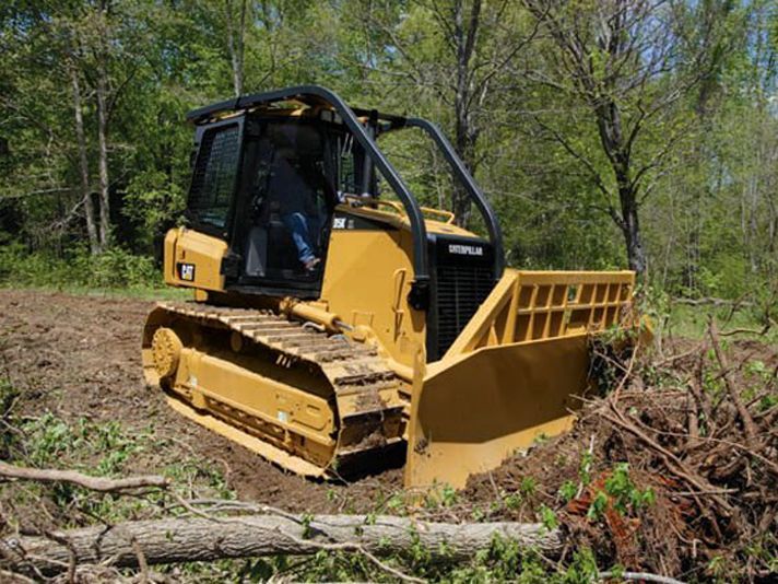 A bulldozer is driving through a forest with trees in the background.