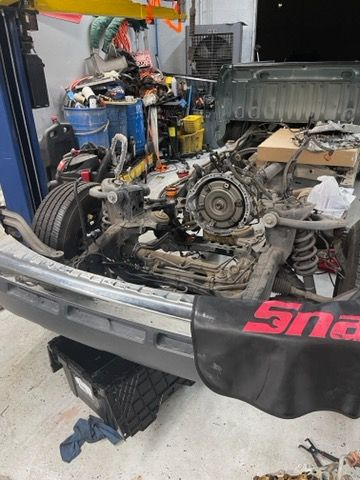 Truck chassis in a shop with engine exposed, on a lift. Shop cluttered with tools and equipment.