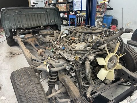 Truck frame with engine, wheels, and bed in an auto repair shop.