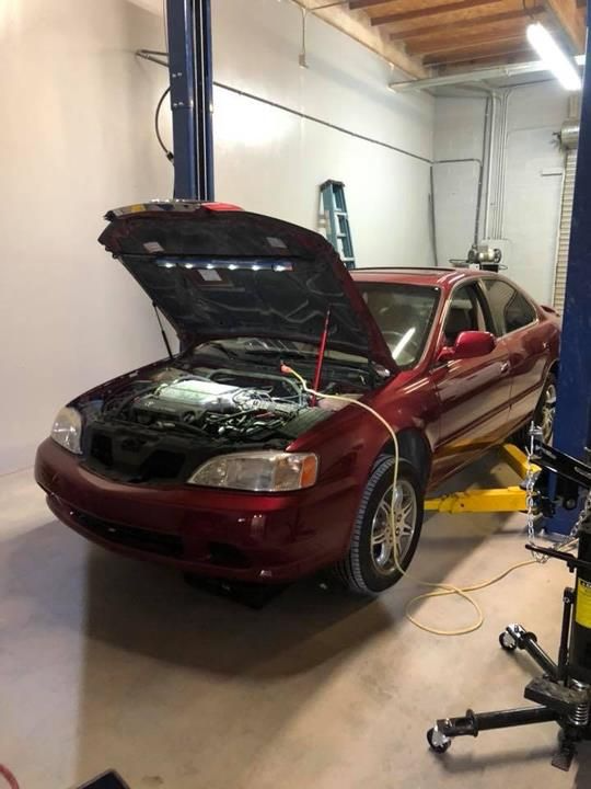Red car with open hood on a yellow lift inside a workshop.