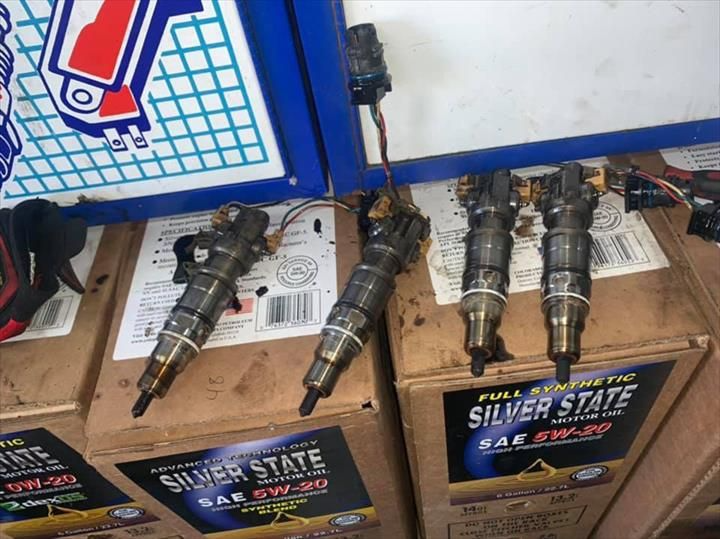 Four diesel fuel injectors on oil boxes, wires attached, shop setting.