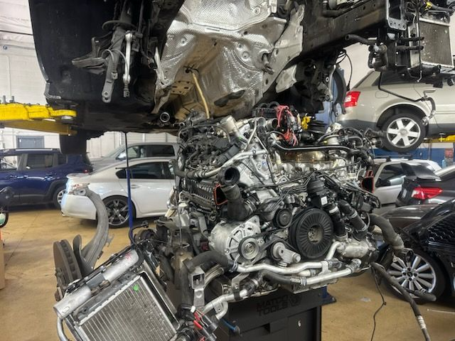 Car engine removed from vehicle in a repair shop, radiator in foreground, other cars in background.