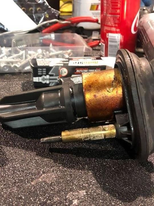 Close-up of a car part, a corroded cylindrical component with a long metal rod attached.