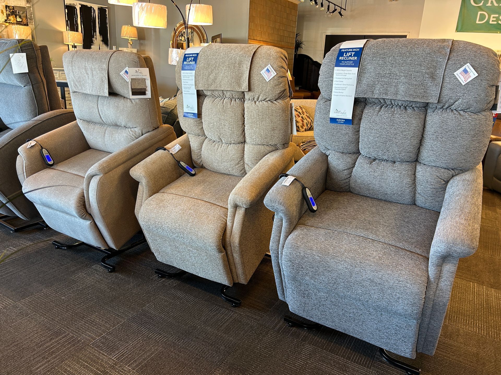 Three gray upholstered recliner chairs displayed in a furniture store showroom.