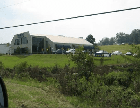 A large white building sits in the middle of a grassy field