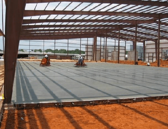 Two men are working on a concrete floor in a large building