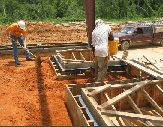 Two men are working on a construction site with a truck in the background