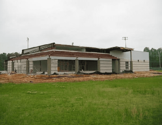 A large white building is being built in a grassy field.