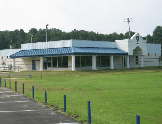 A white building with a blue roof is surrounded by a lush green field