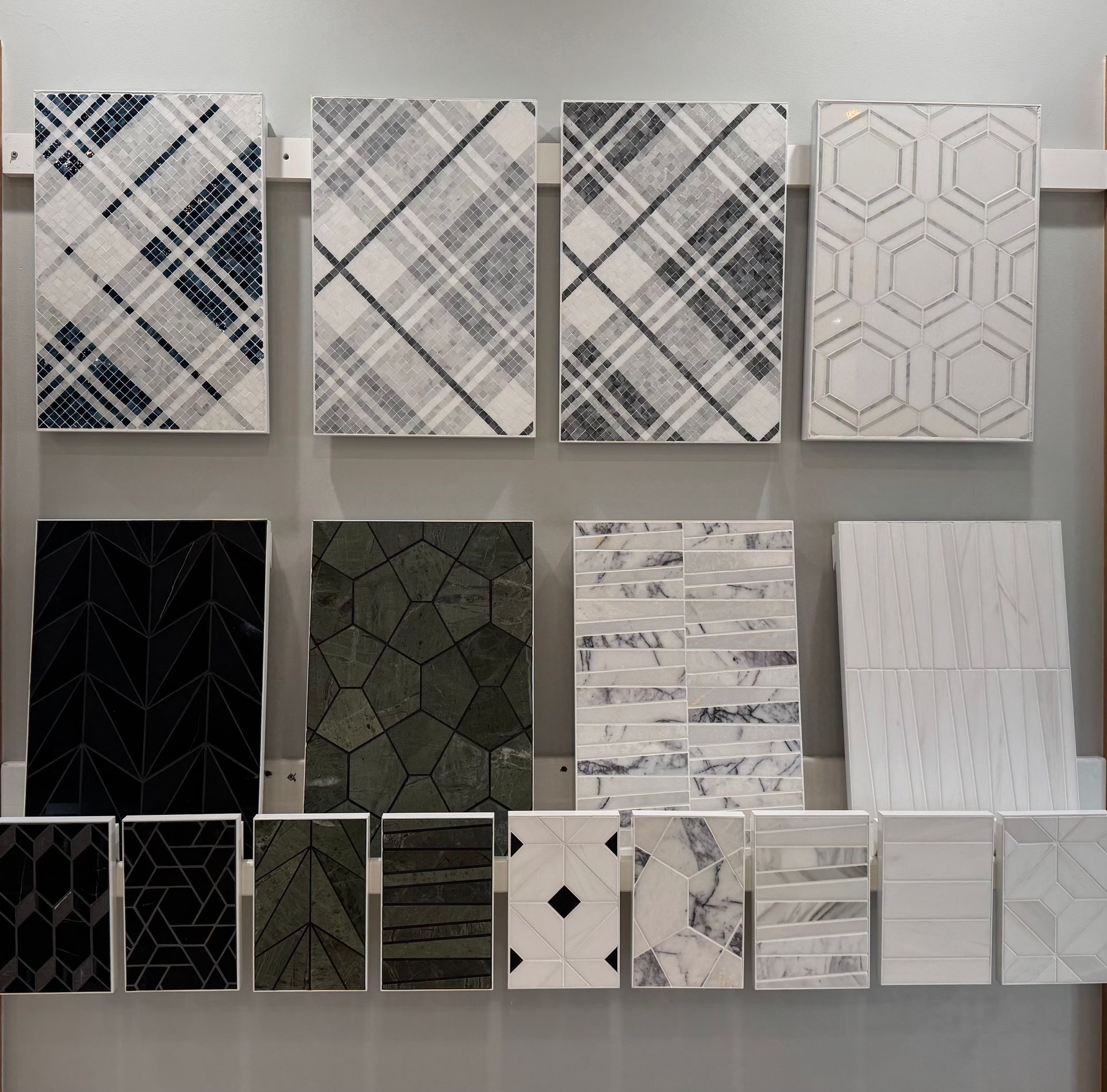 A display of various tile samples on a wall. The tiles feature a range of patterns and colors, including plaid, geometric, and natural stone.