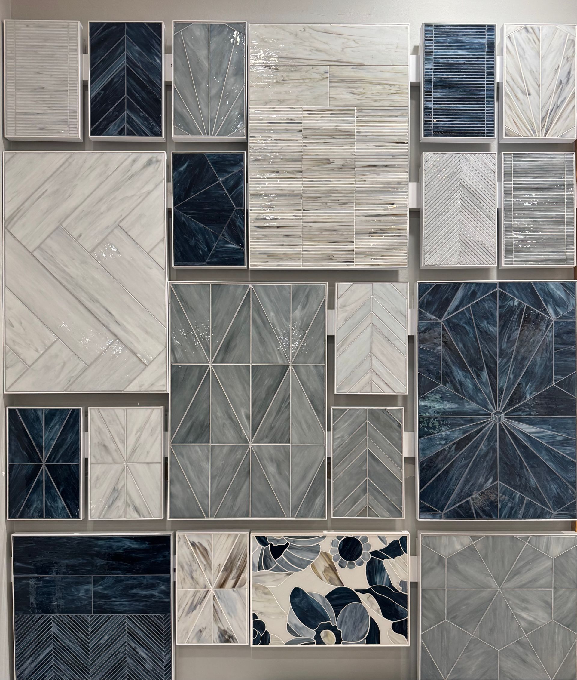 Display of various blue and gray tile samples arranged on a wall, showcasing diverse patterns and textures.