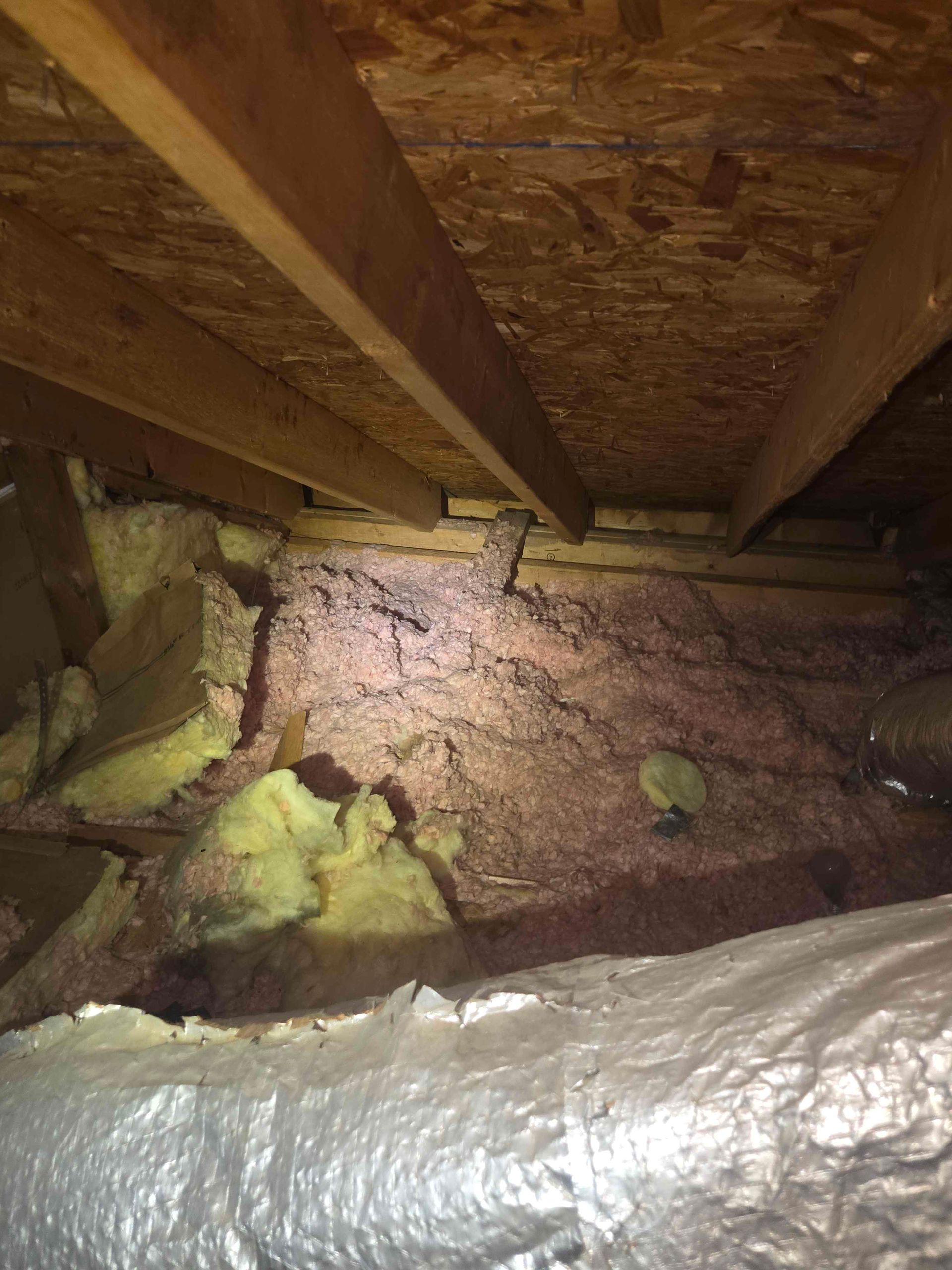 Attic with pink insulation, wooden beams, ductwork, and a silver vapor barrier.