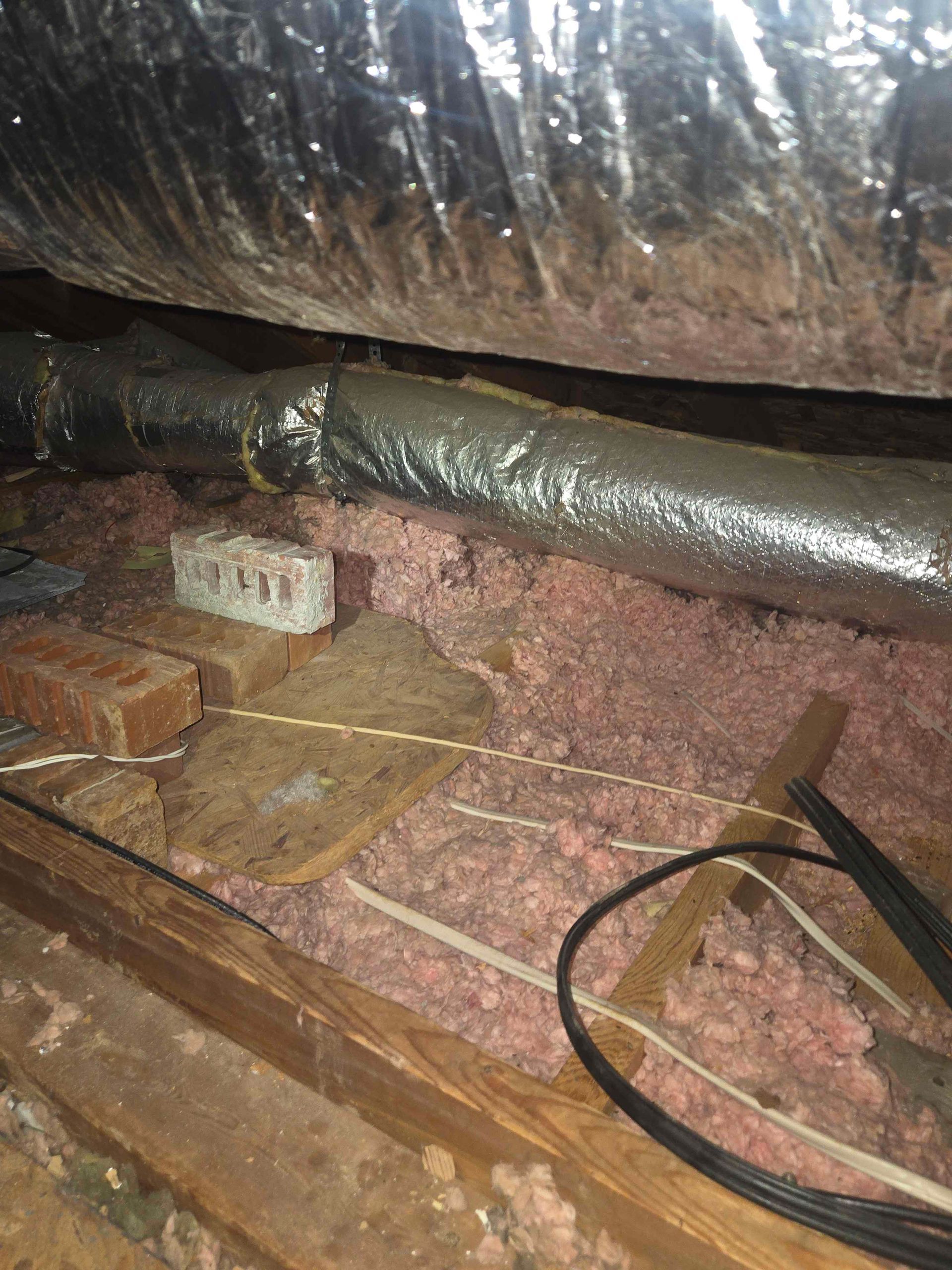 Pink insulation and brick supports under ductwork in an attic. Wires visible.