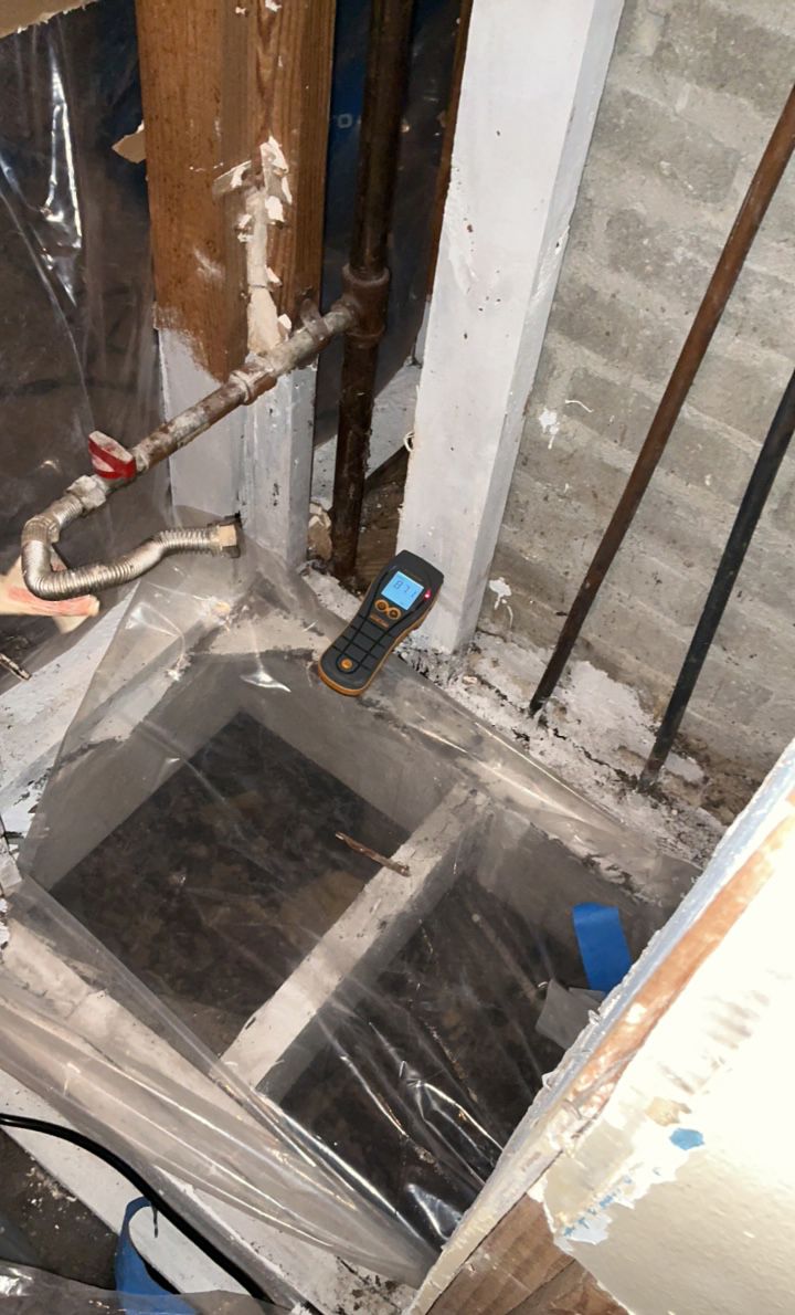 A close-up shot of a moisture meter near pipes and a concrete opening.