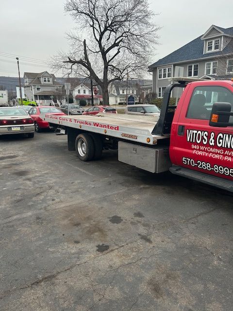 A red tow truck from Vito's & Gino's is parked in a parking lot