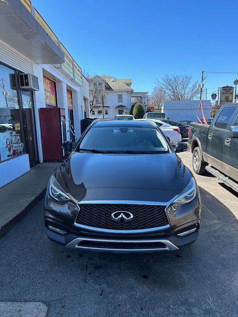 A brown Infiniti QX30 is parked in a parking lot in front of a building.