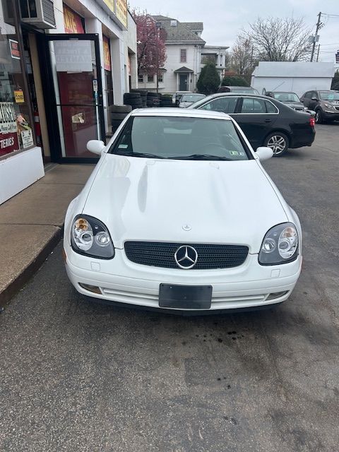 A white mercedes is parked in a parking lot in front of a store